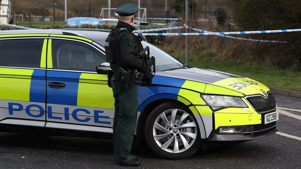 PSNI officer standing in front of a car holding a gun