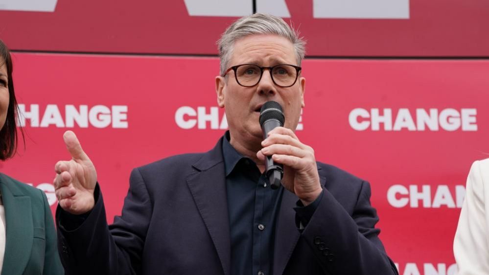 Keir Starmer speaks into a microphone in front of a red backdrop