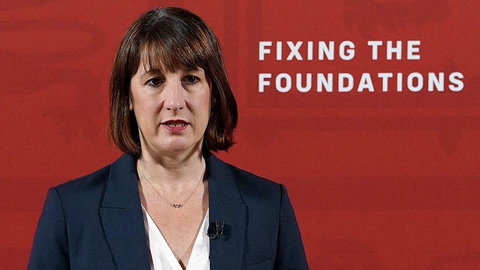 Rachel Reeves stands in front of a red wall at a press conference