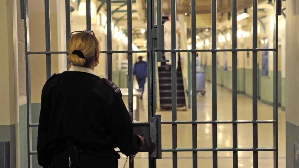 Female prison warder stands near gated door in London prison