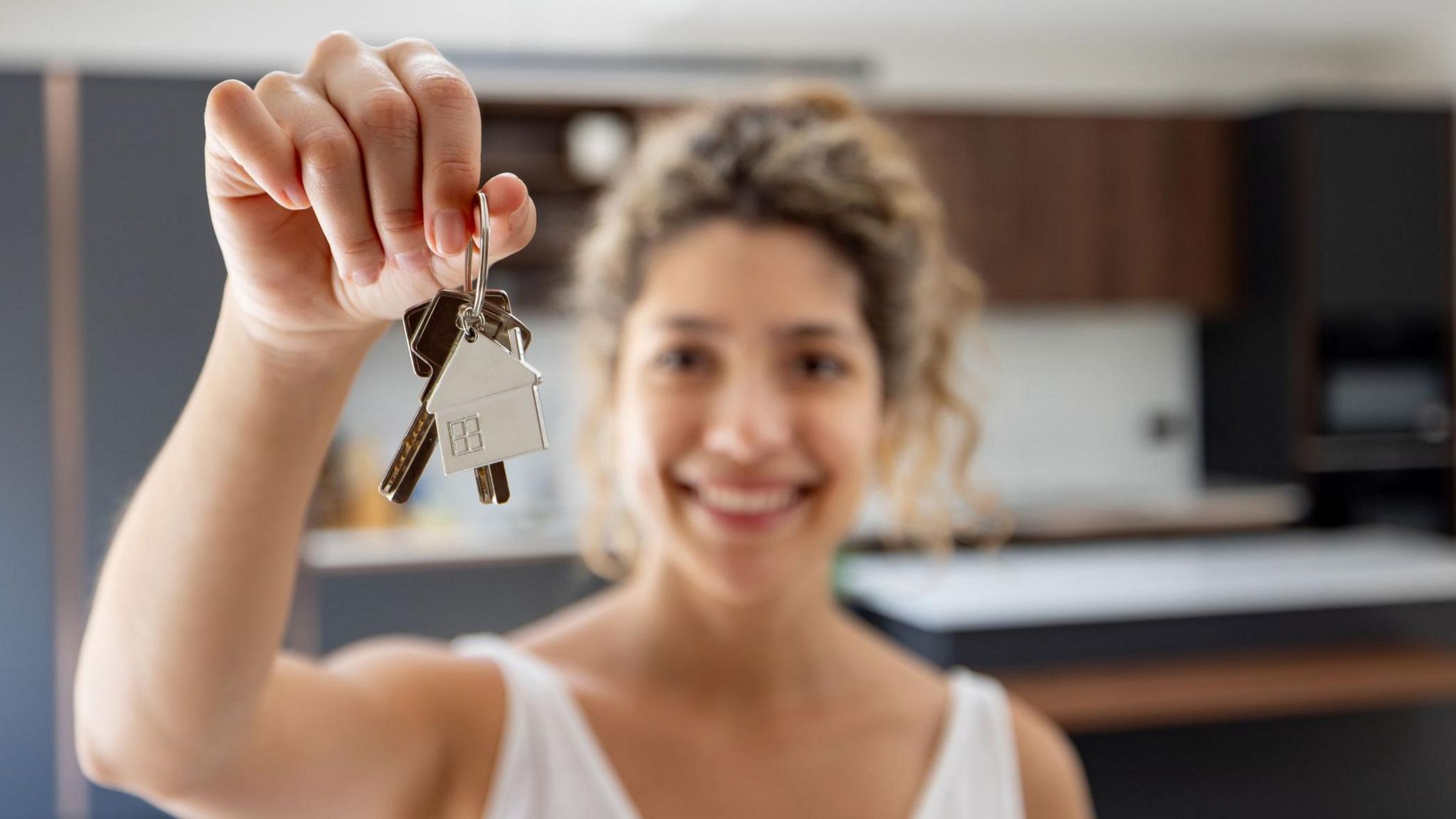 Happy woman holding keys while looking at the camera smiling