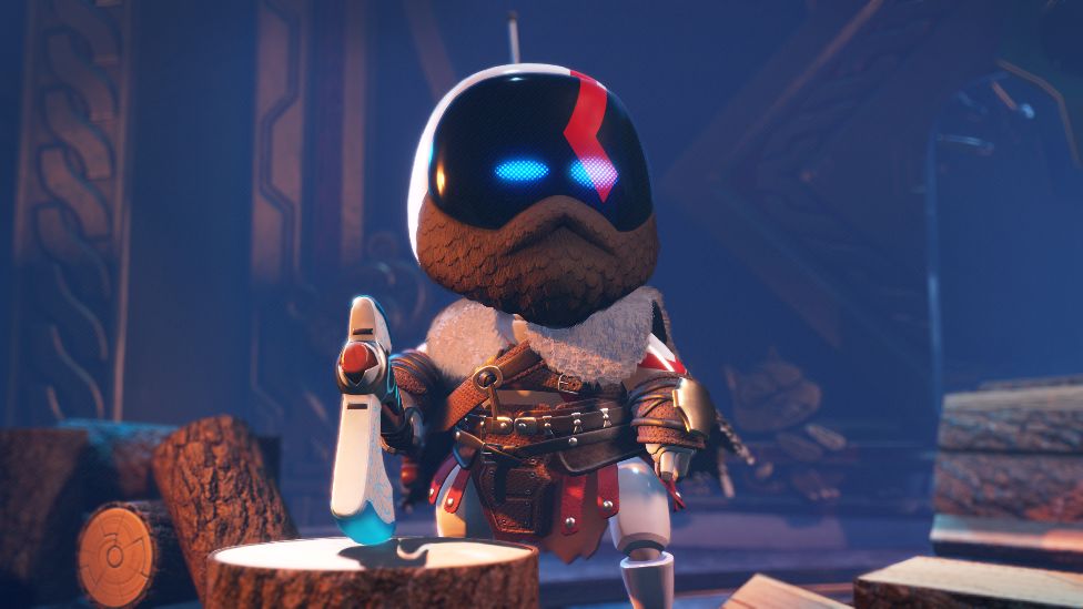 A screenshot of Astro Bot - a white, cute robot with light blue eyes - dressed to resemble Kratos, the protagonist from God of War. Astro has a beard, and wears a leather outfit with lots of buckles and a fur collar. Astro stands next to a chopping block, holding a large axe and is surrounded by logs.