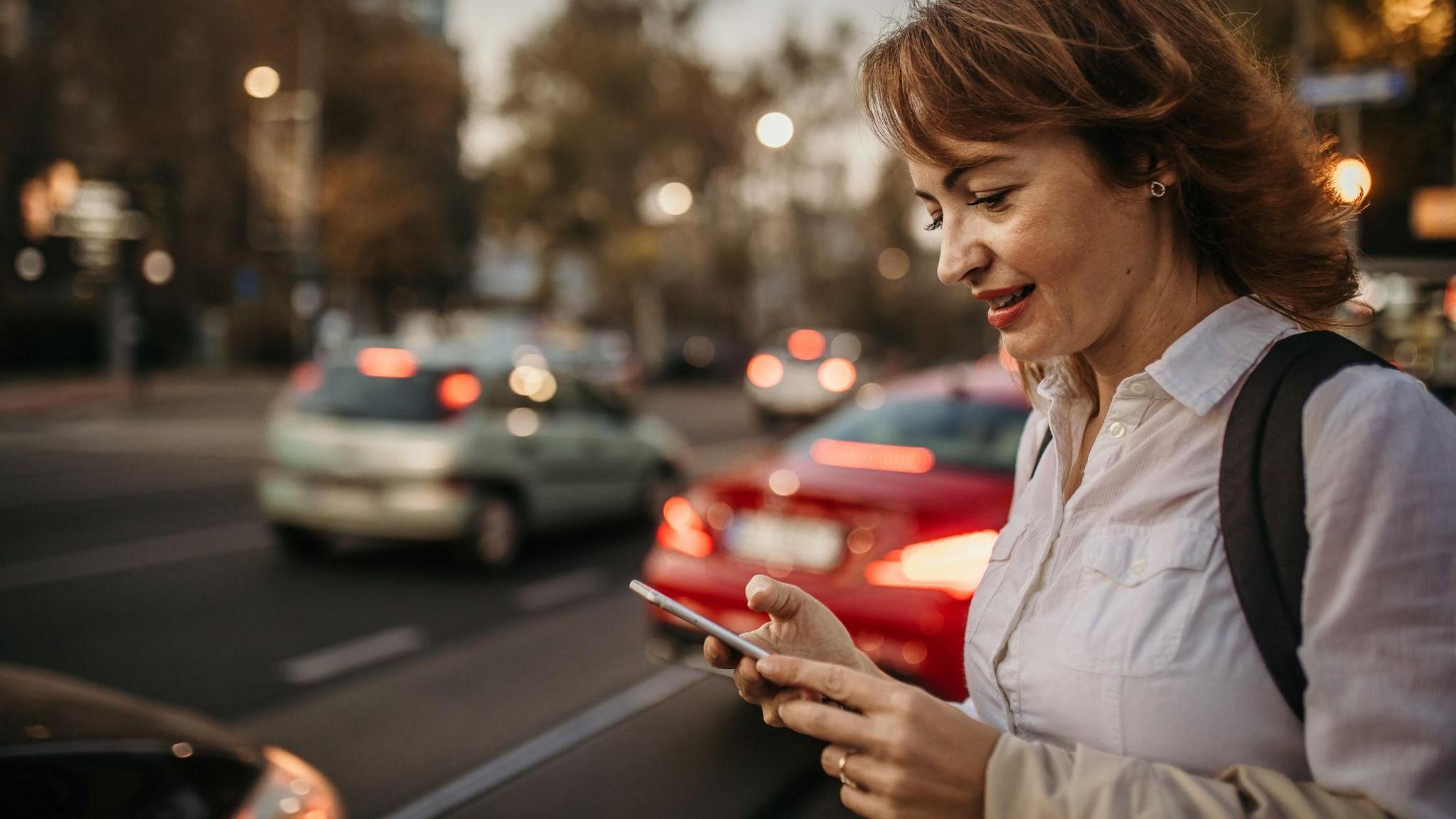 Woman by a busy road looking at her phone waiting for a ride