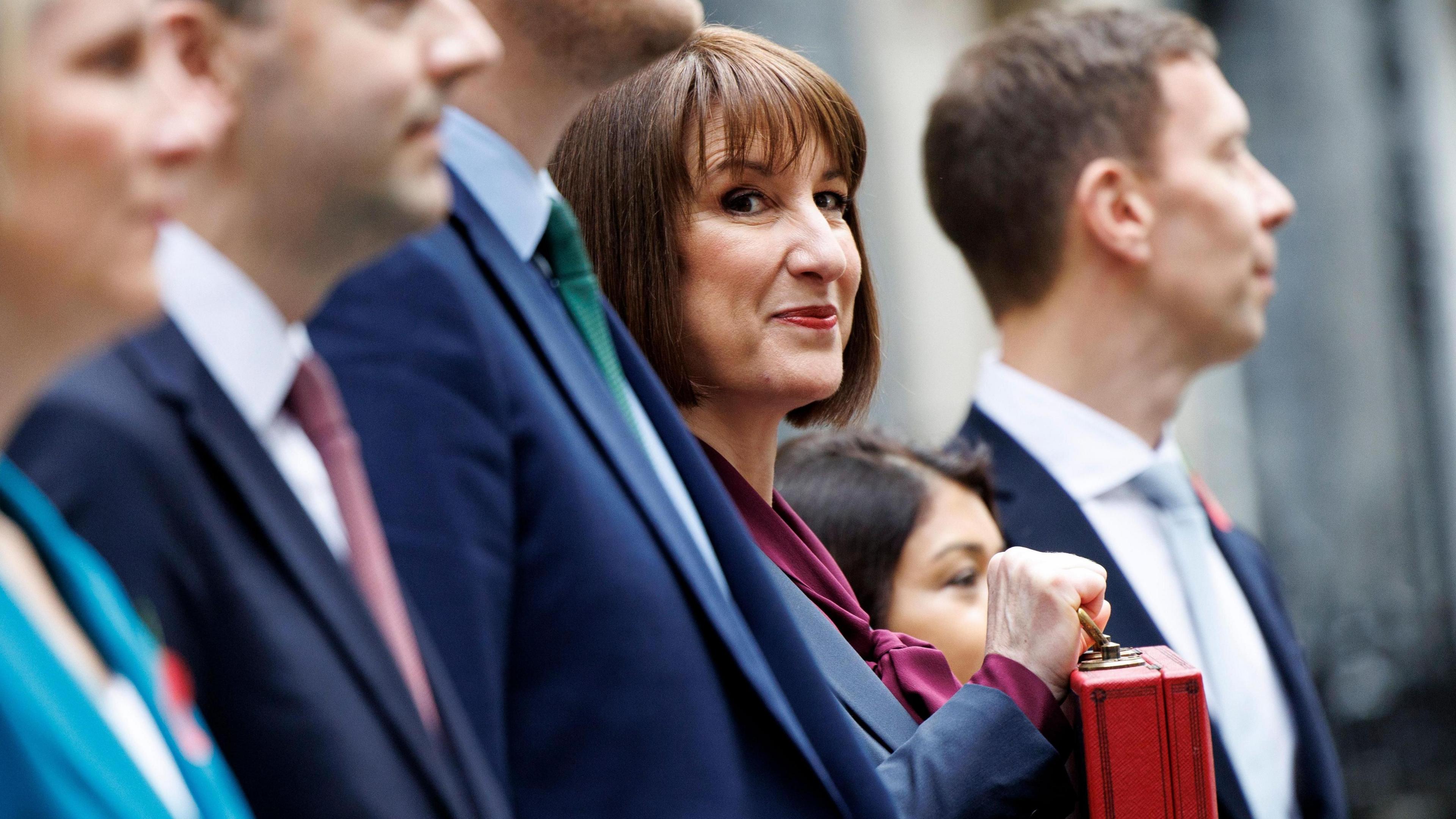 Rachel Reeves poses for the cameras with a line up of her Treasury ministers. She is smiling and holding the traditional Budget red box