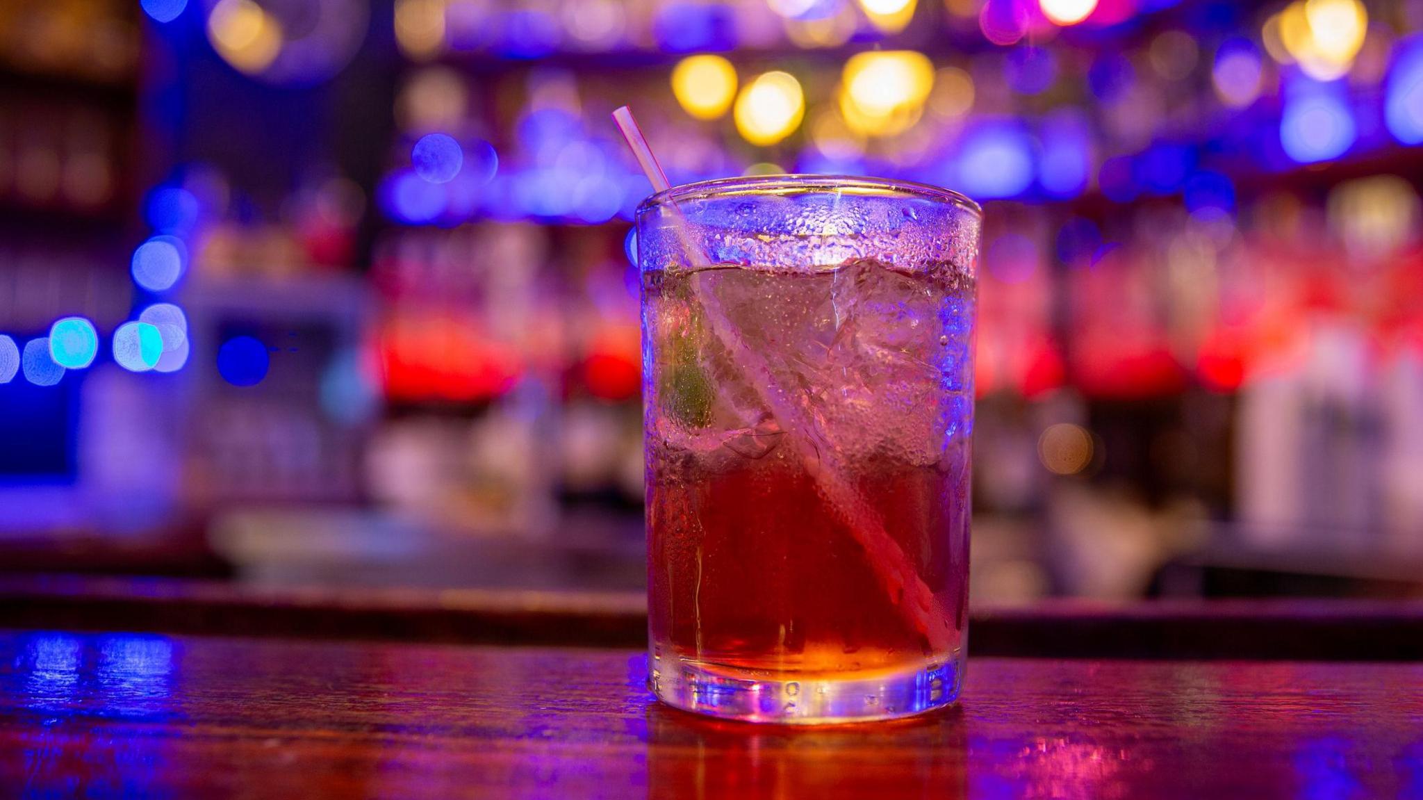 A mixed drink sits on a wooden bar top with the bar in the background out of focus