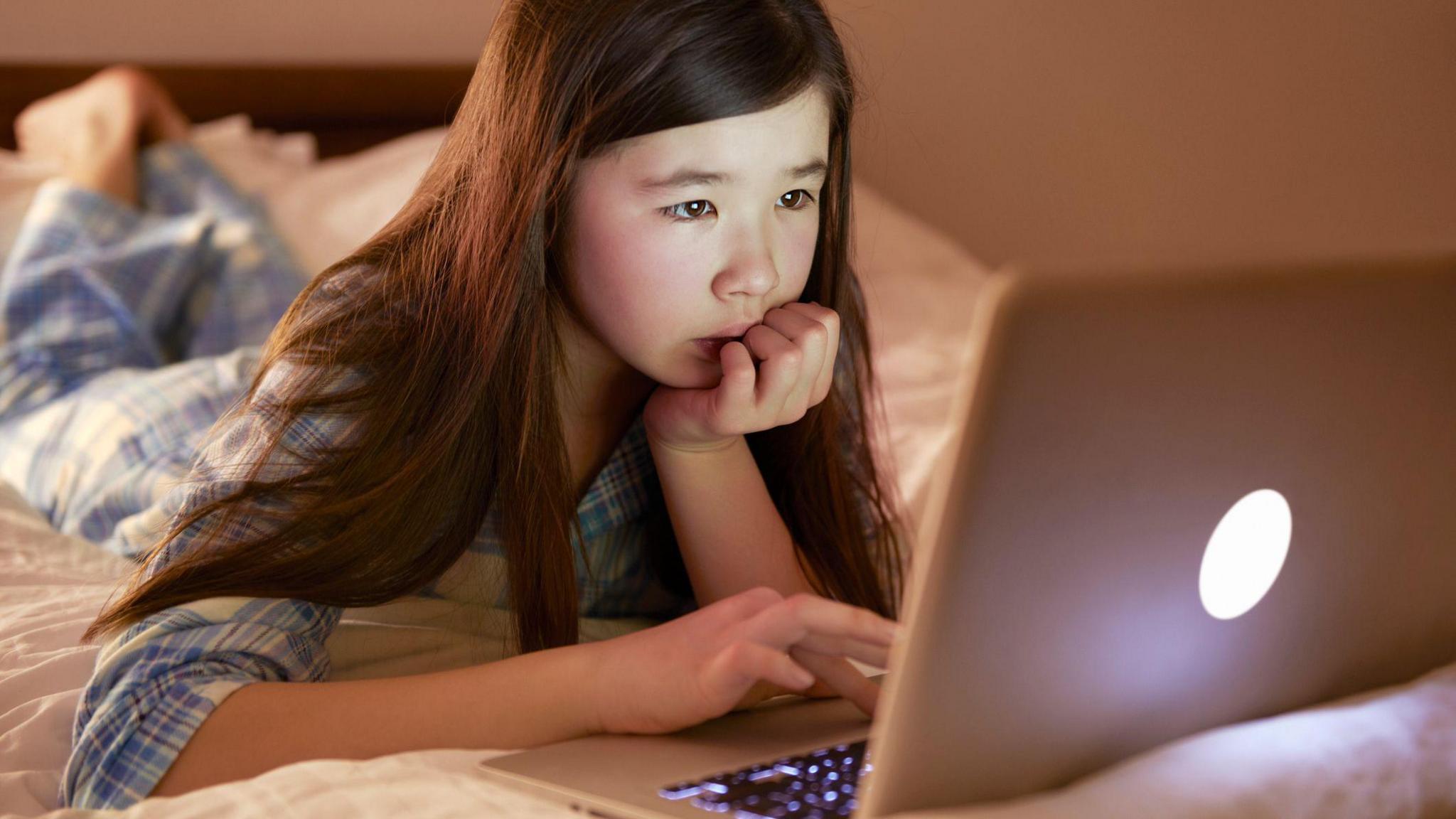 A young child looks curious as she uses a laptop.