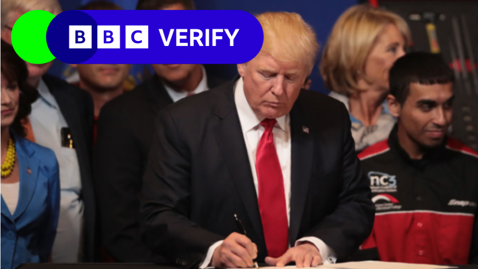 Trump is a dark suit and red tie signs a document