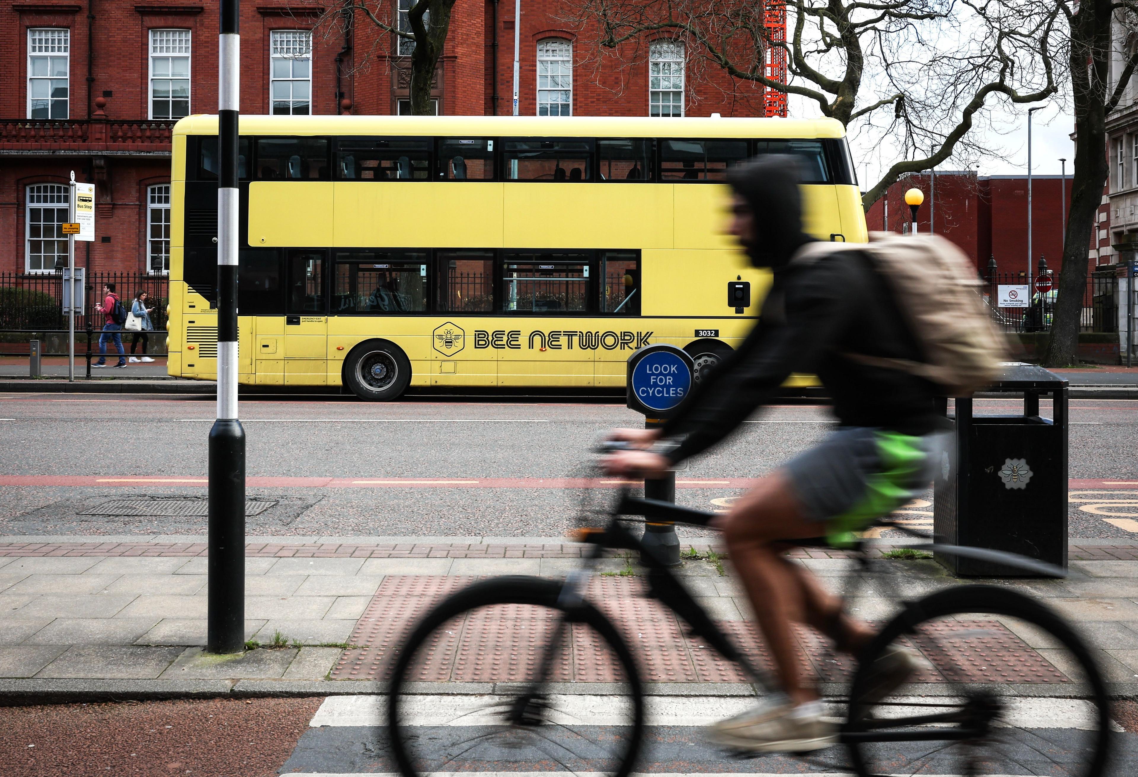 A cyclist in the foreground rides past a yellow, bee network branded bus in the background.