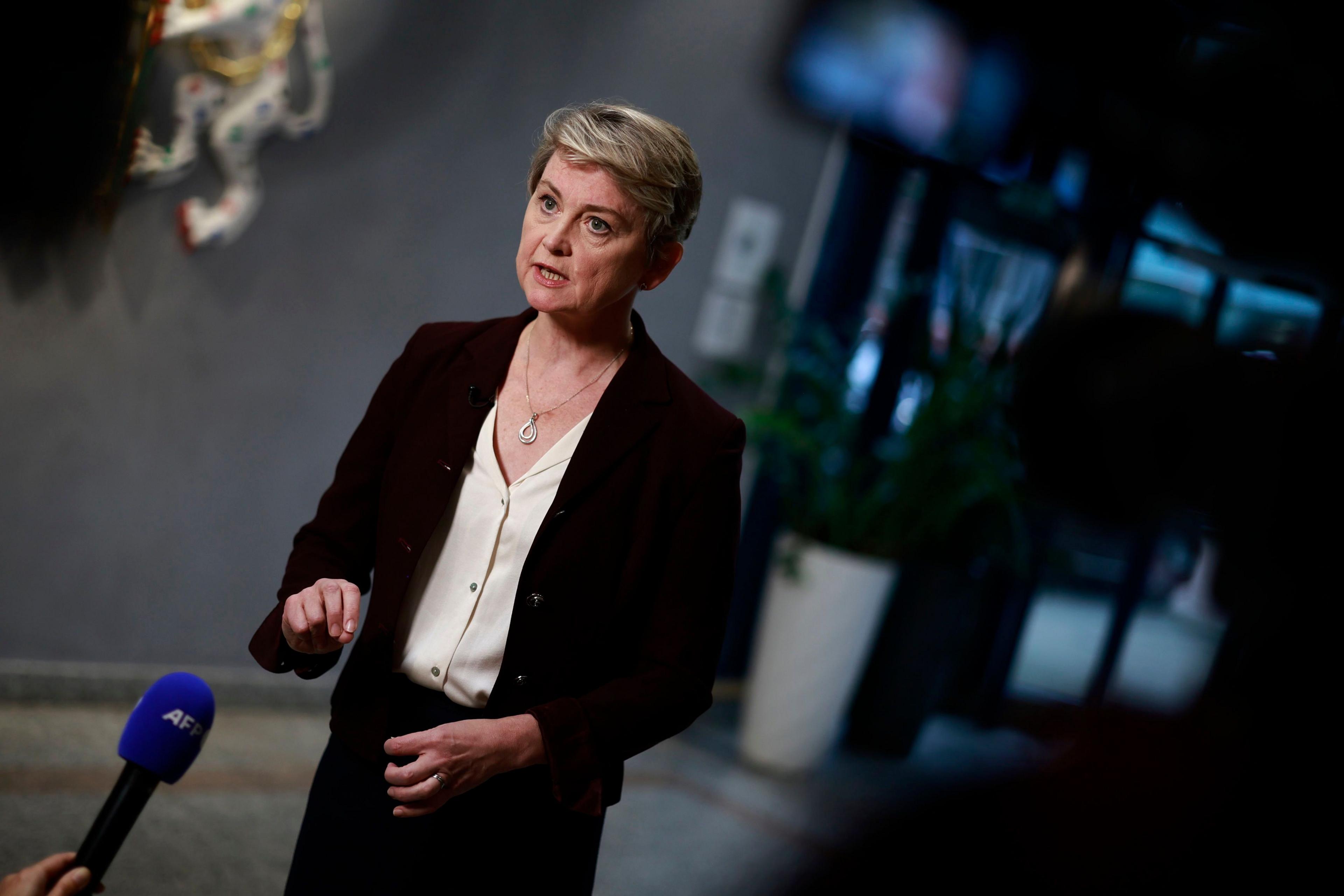 Home Secretary Yvette Cooper wearing a black blazer and white blouse speaks into a microphone during a press conference 