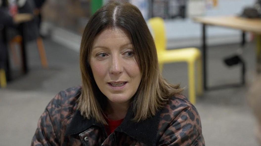 Nicola Price wearing a leopard print jacket over a red T-shirt, with a desk and a yellow chair seen behind her