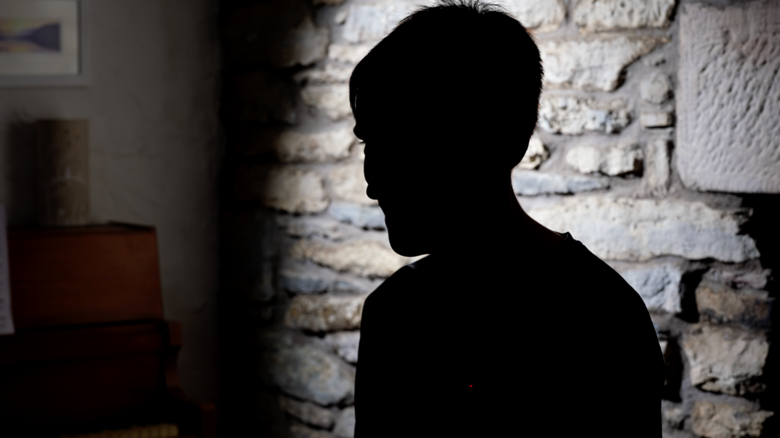 ilhouette of a teenager sitting in profile against a stone wall.