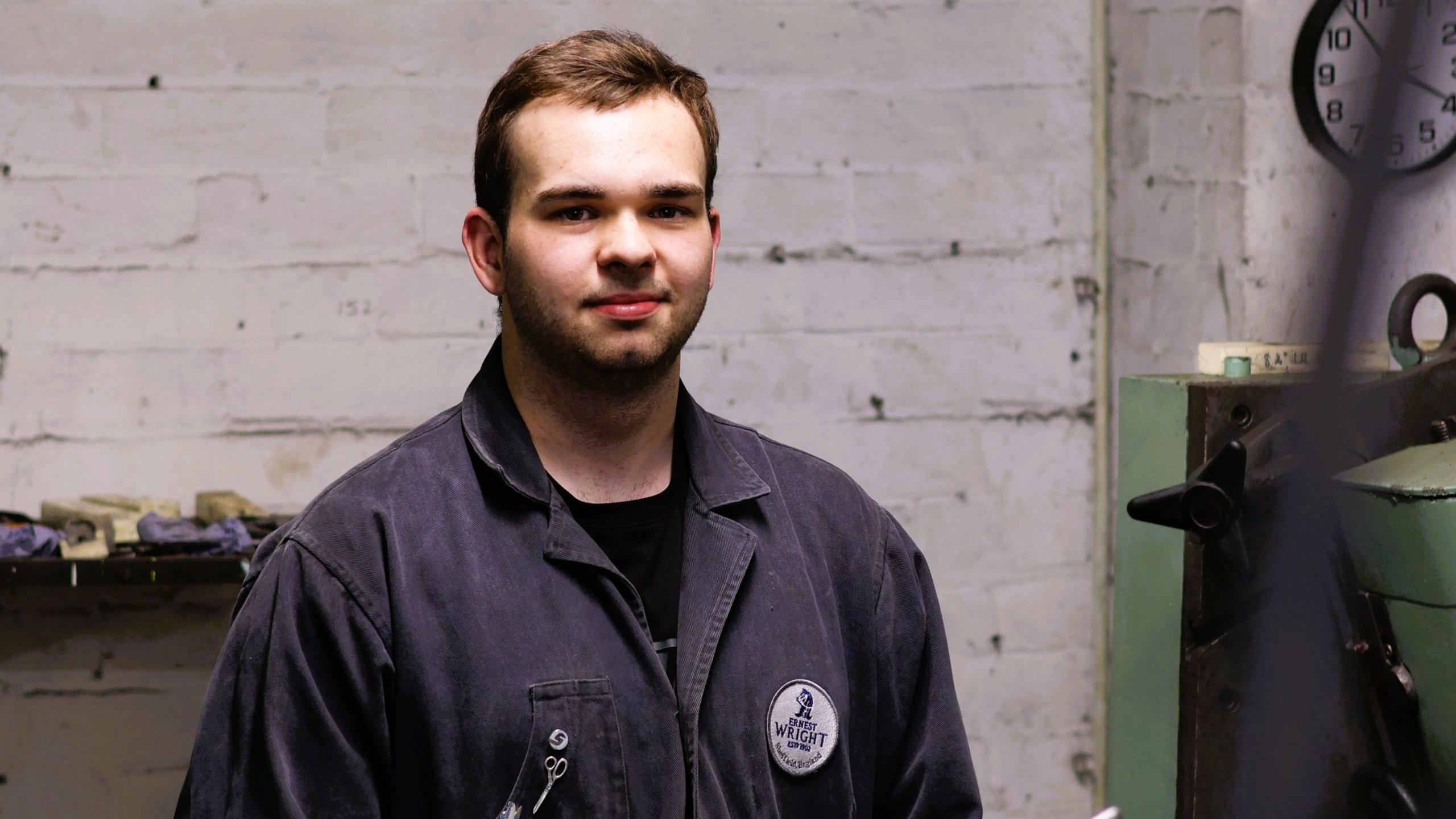 Elliott Nurcombe in a blue boiler suit stands in the Ernest Wright workshop
