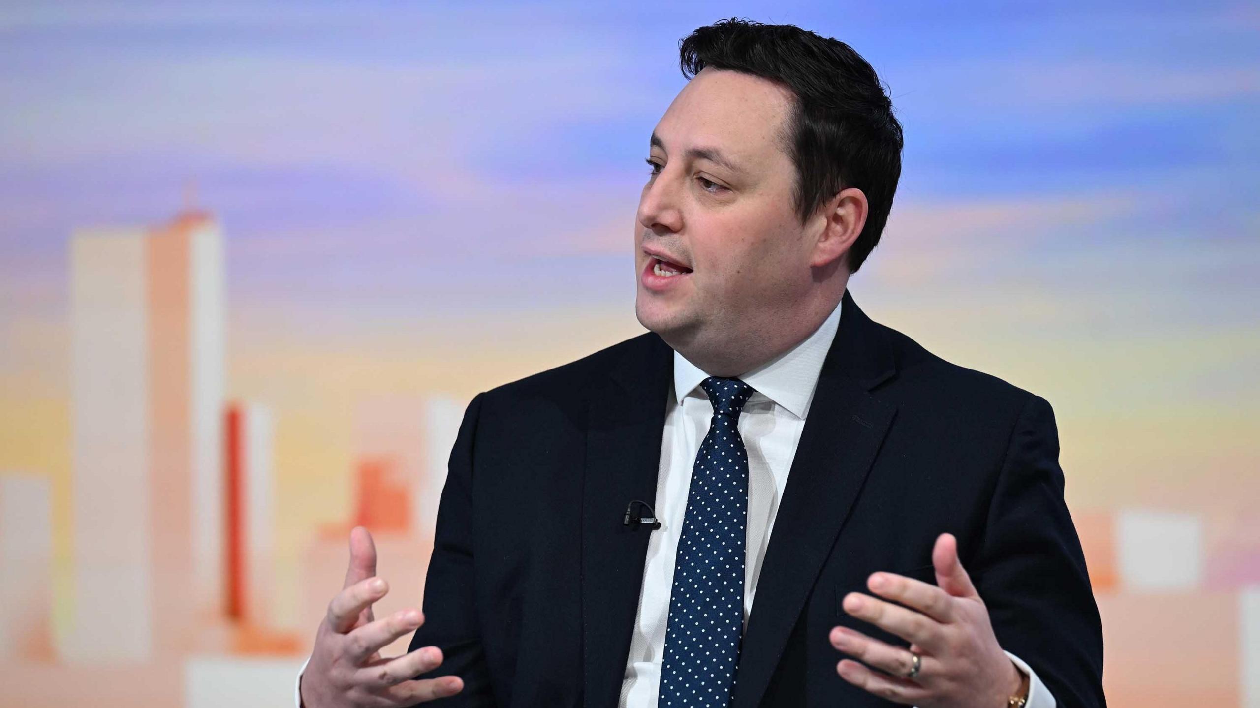 Ben Houchen, in a dark suit and tie, makes a point with his hands in a TV studio debate