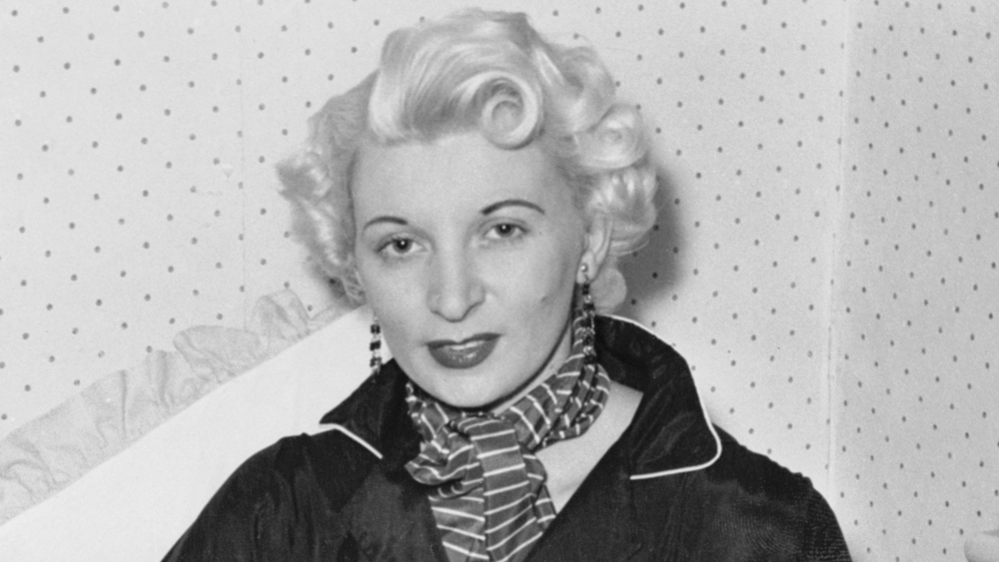 Ruth Ellis poses for a photograph - the black and white picture shows her with white-blonde hair, wearing long earrings, a striped scarf and a black shirt.