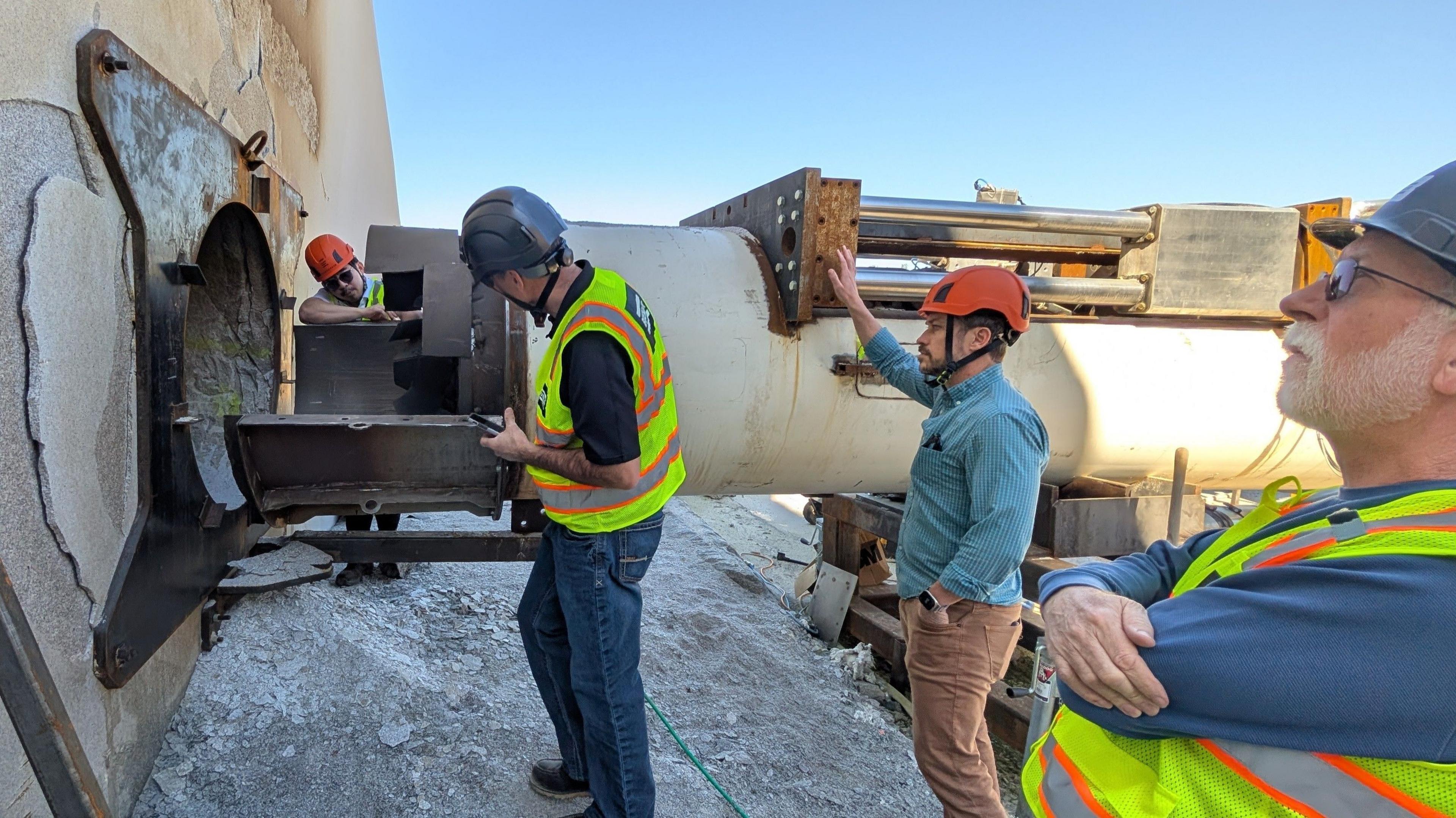 Four engineers stand close to a large metal cylinder which containers the Earthgrid boring machine. 