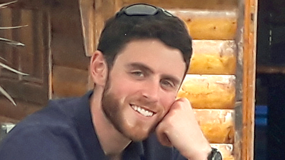PC Harper looks relaxed as he rests his face on one hand while seated and smiling. He has sunglasses pushed back over his head.