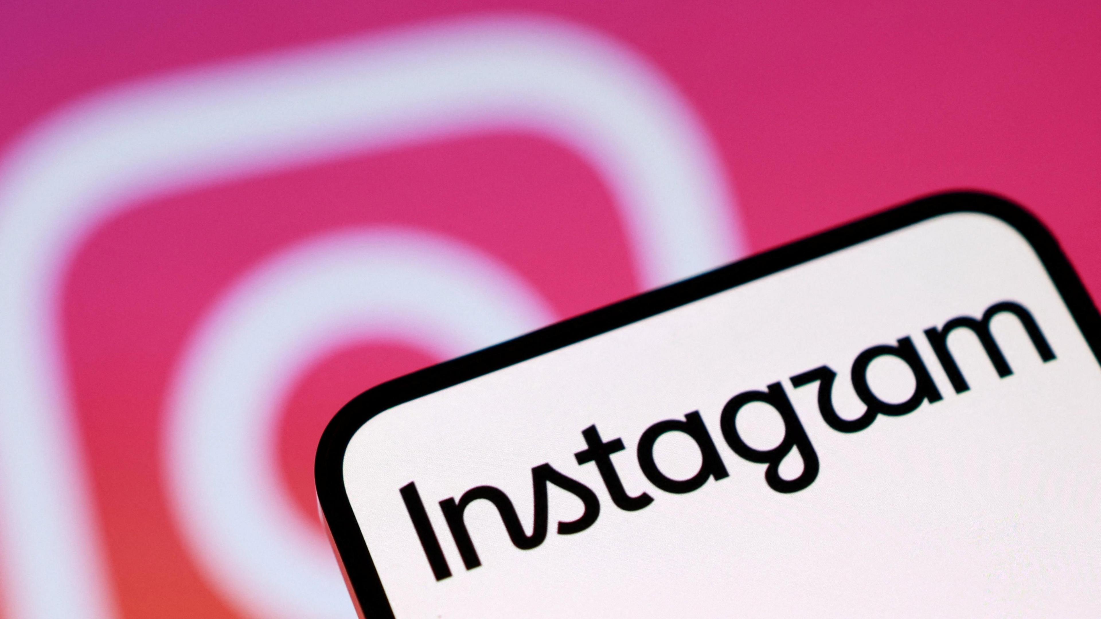 A phone screen with Instagram written on it. In the background is the pink and white Instagram camera logo