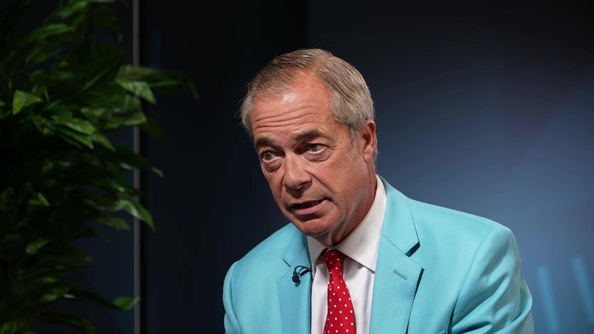 Nigel Farage wears a bright blue suit and red tie.