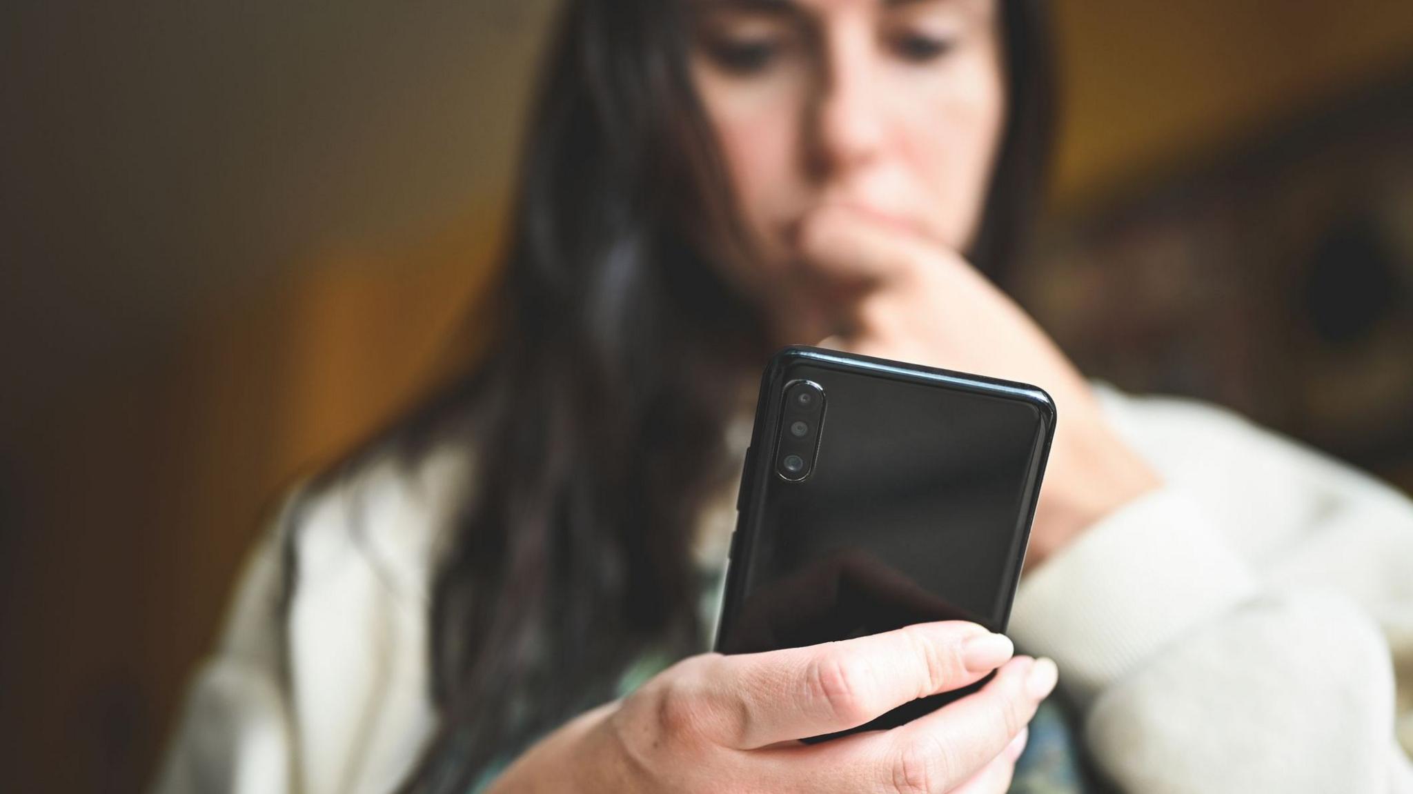 A stock image of a woman looking down at her smartphone, biting her nails nervously