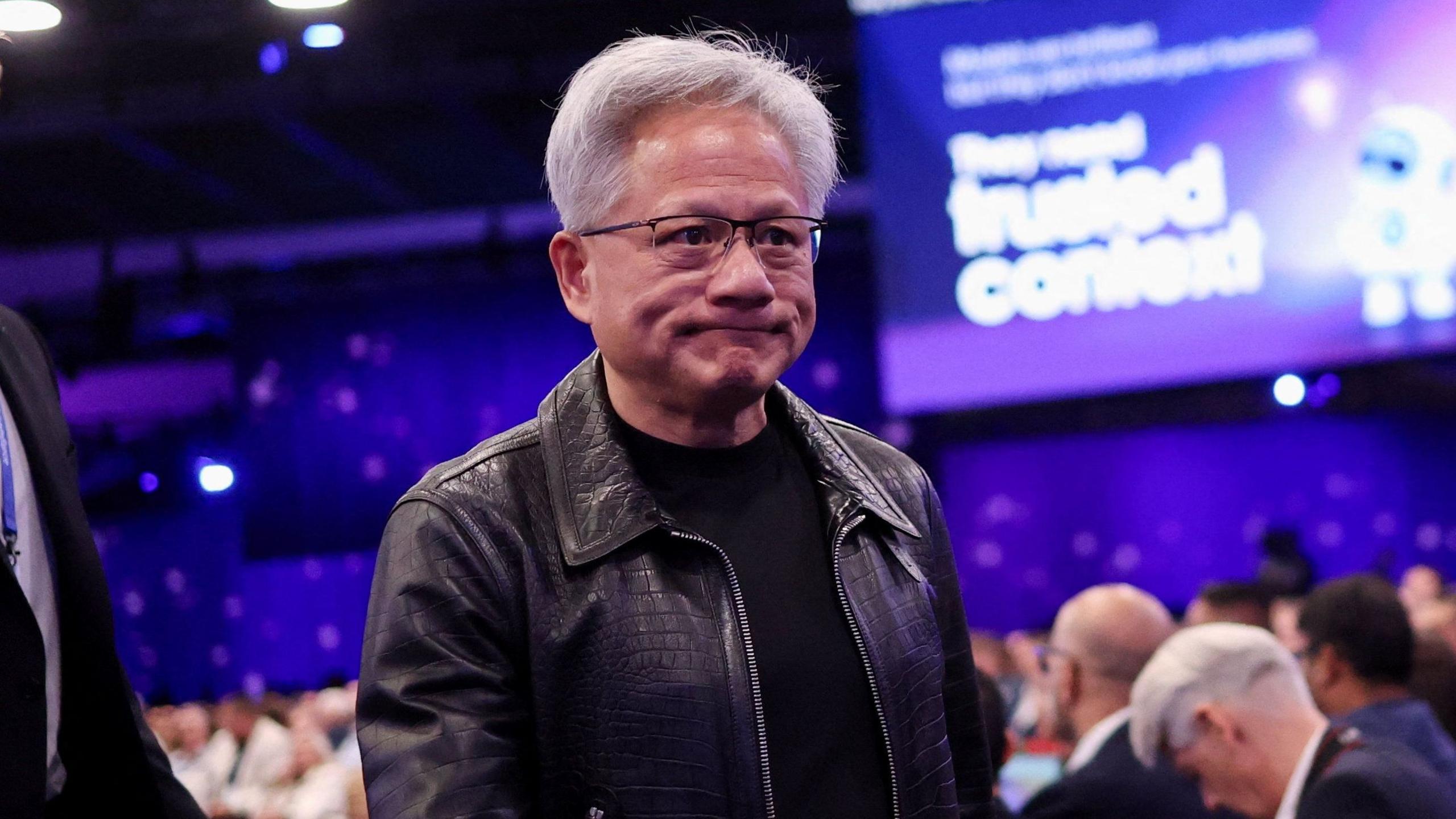 Nvidia CEO Jensen Huang walking the floor at the Salesforce "Dreamforce" conference, wearing a black leather jacket and black t-shirt.  