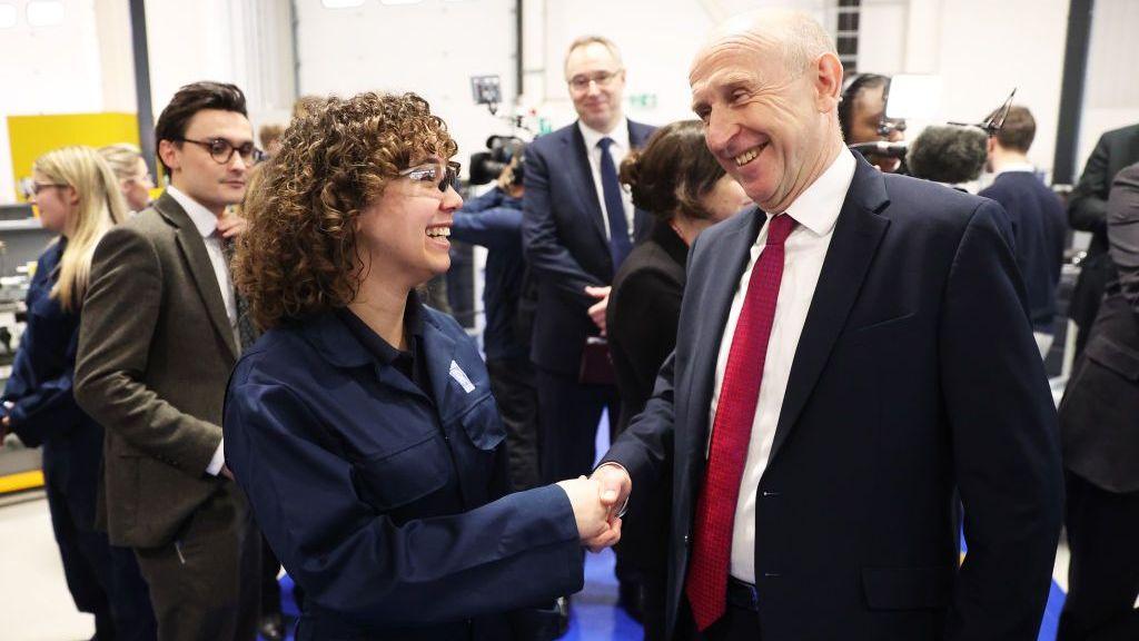 John Healey shakes hands with a young female apprentice in a lab.