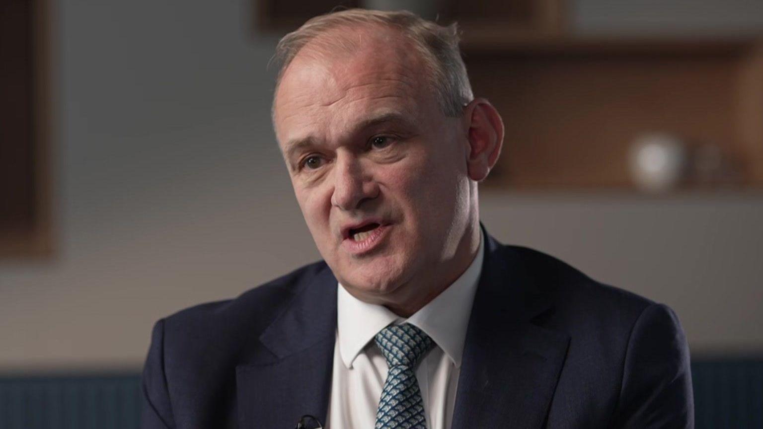 Head and shoulders shot of Davey, who is wearing a navy siut jacket, a white shirt and a blue and green patterned tie.