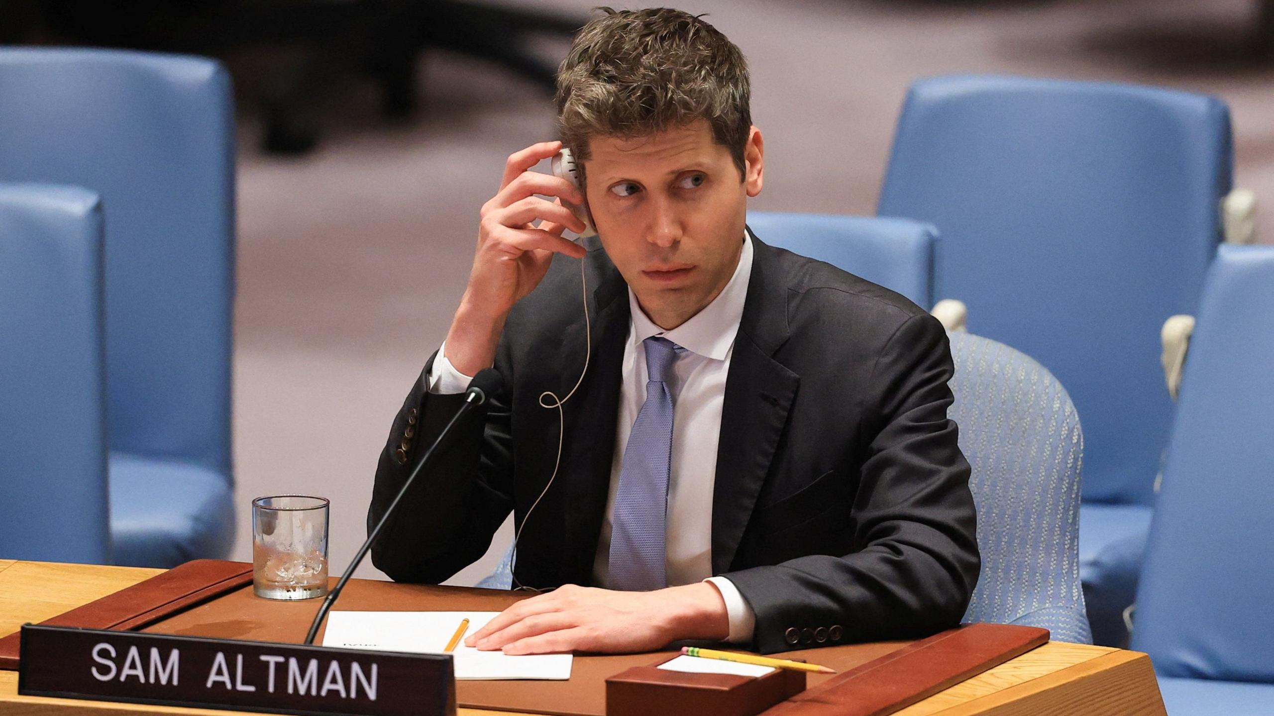 Sam Altman of OpenAI sitting before the US Security Council wearing a suit and tie while listening to a translation of comments.