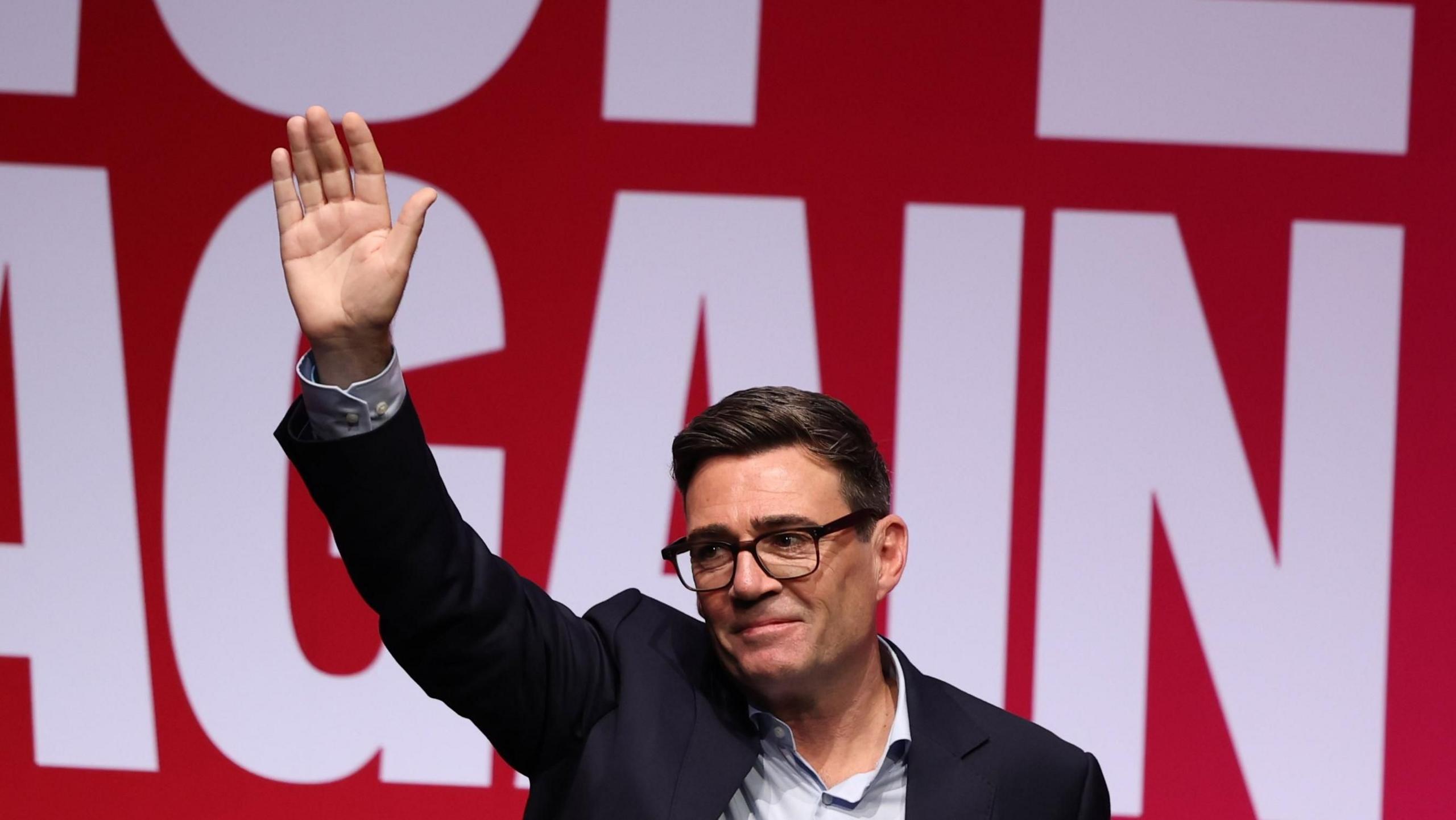 Andy Burnham waves to the audience in Liverpool against a "Hope Again" banner in the background