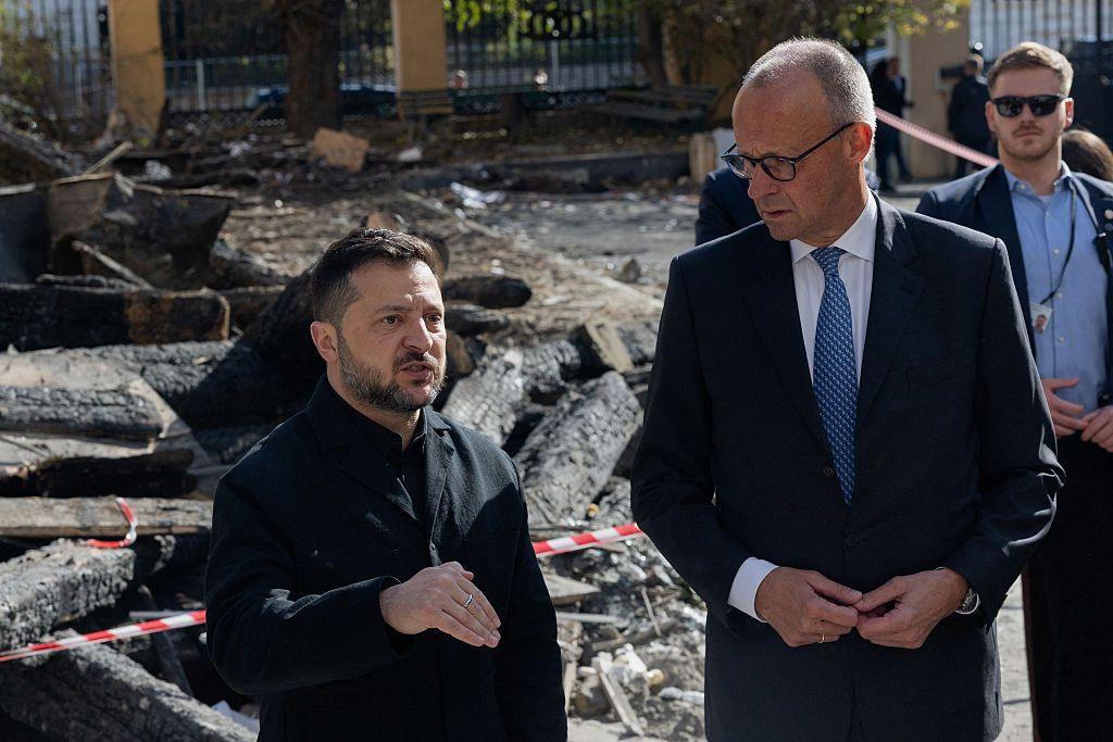 Ukrainian president Volodymyr Zelensky and German Chancellor Friedrich Merz stand alongside each other while speaking to reporters in front of cordoned-off rubble in Kyiv.