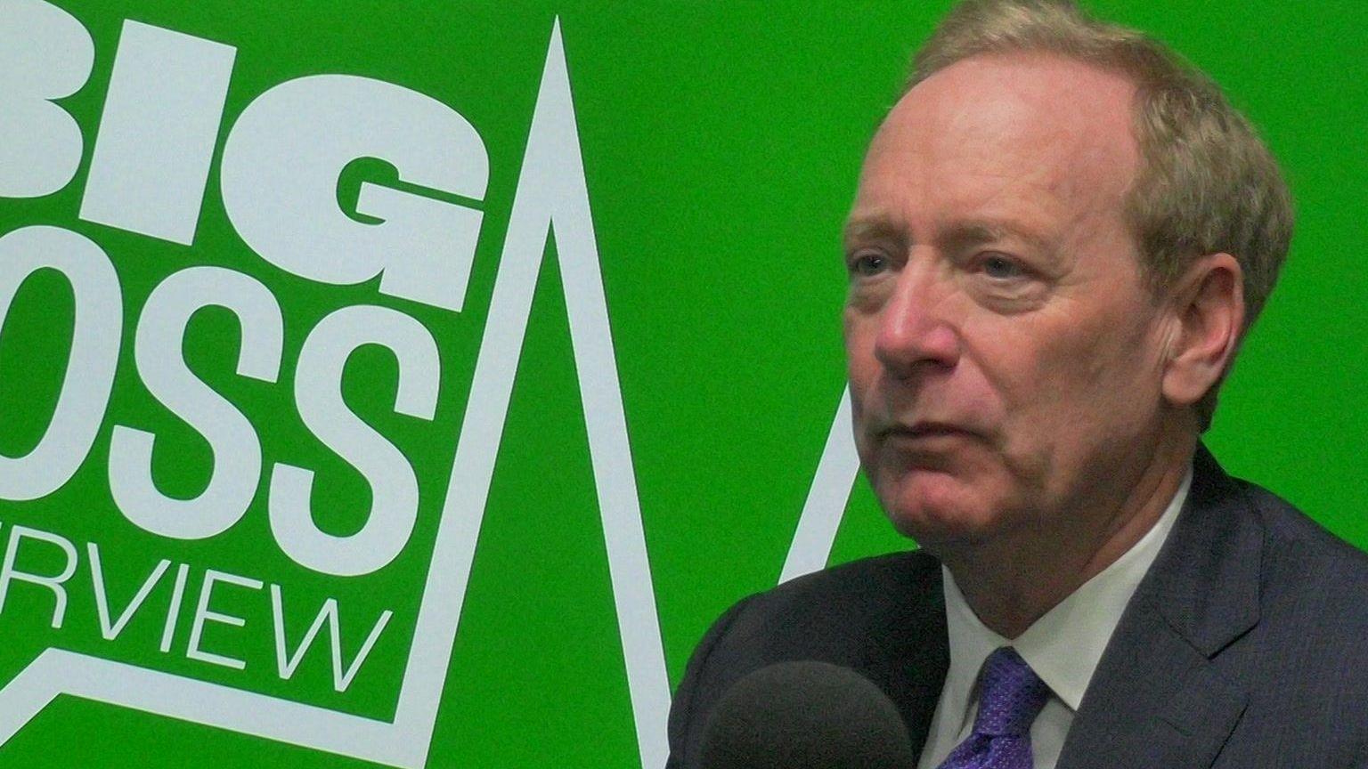 Microsoft president Brad Smith sitting in front of a microphone in a radio studio with Big Boss Interview written on a green background behind him