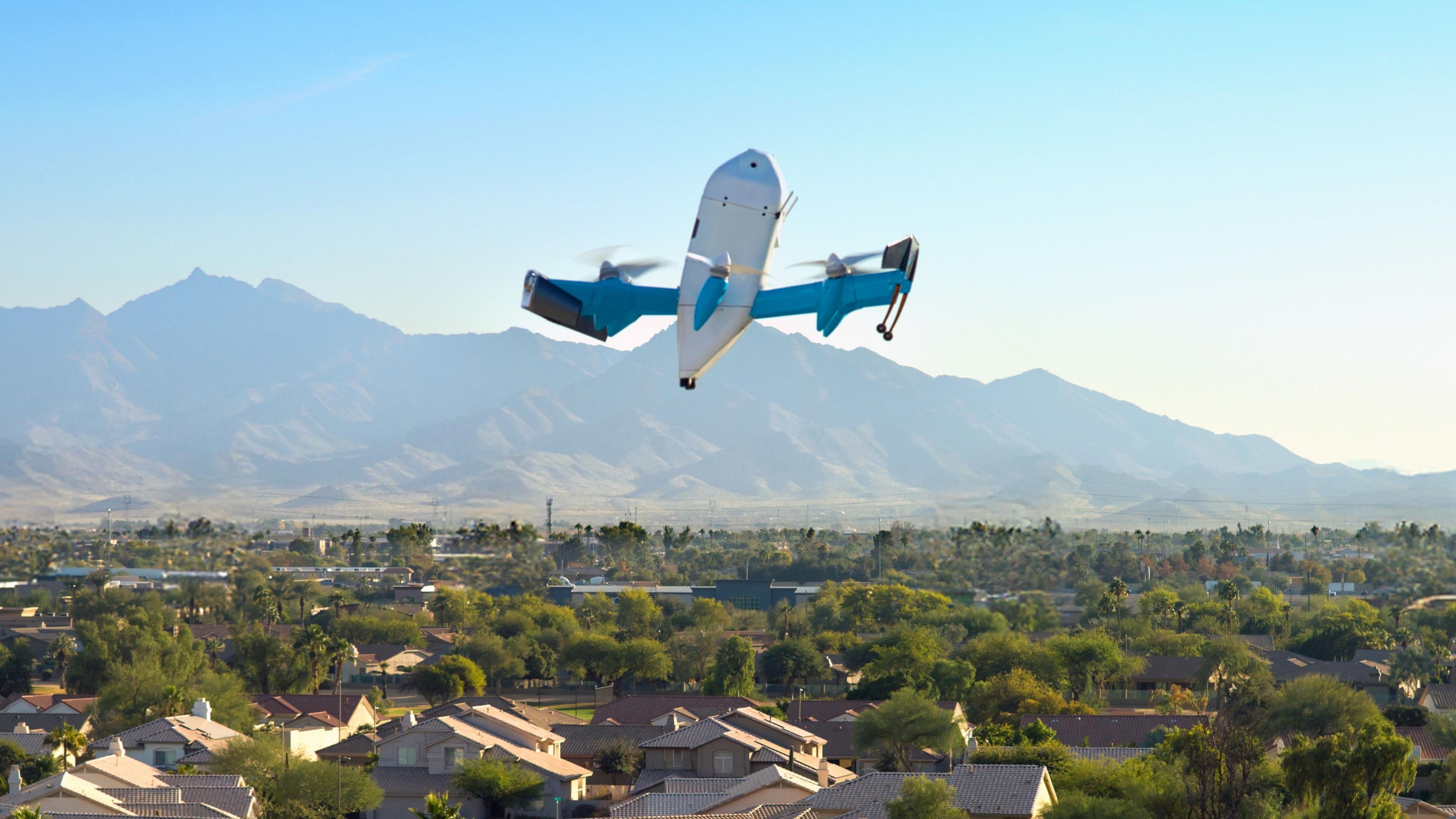 An Amazon drone flies over an US city. In the background are mountains and a blue sky.