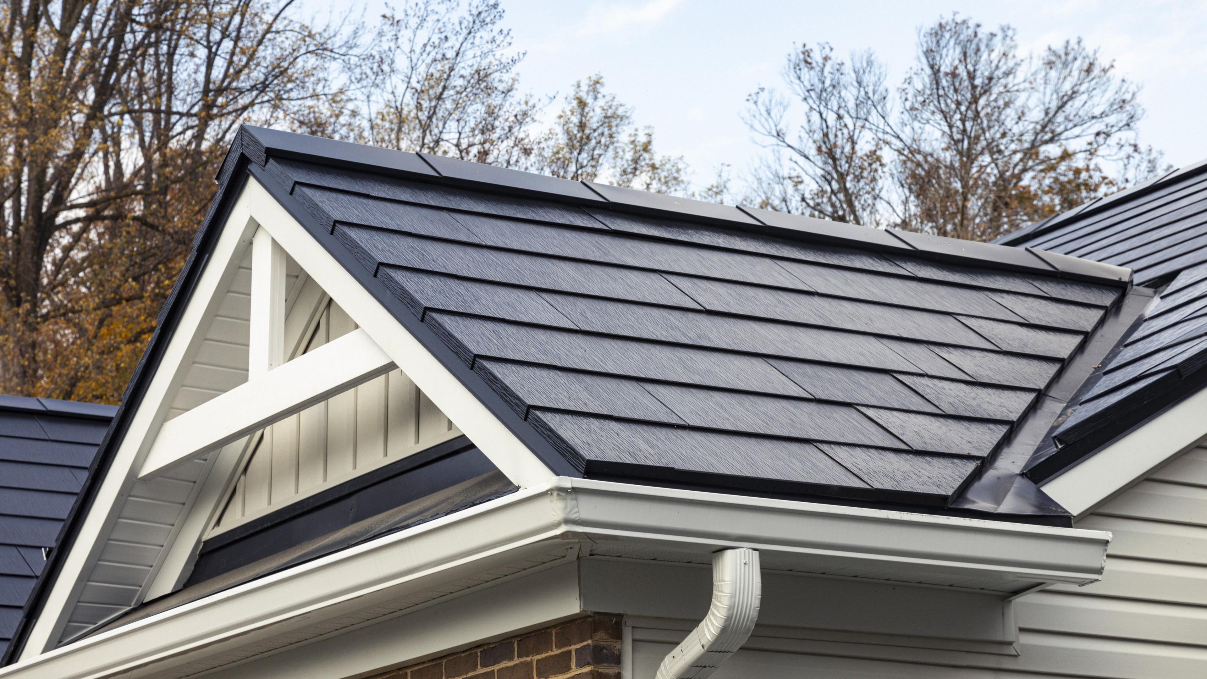 Black Tesla solar tiles on a roof. They look like thicker versions of regular tiles.