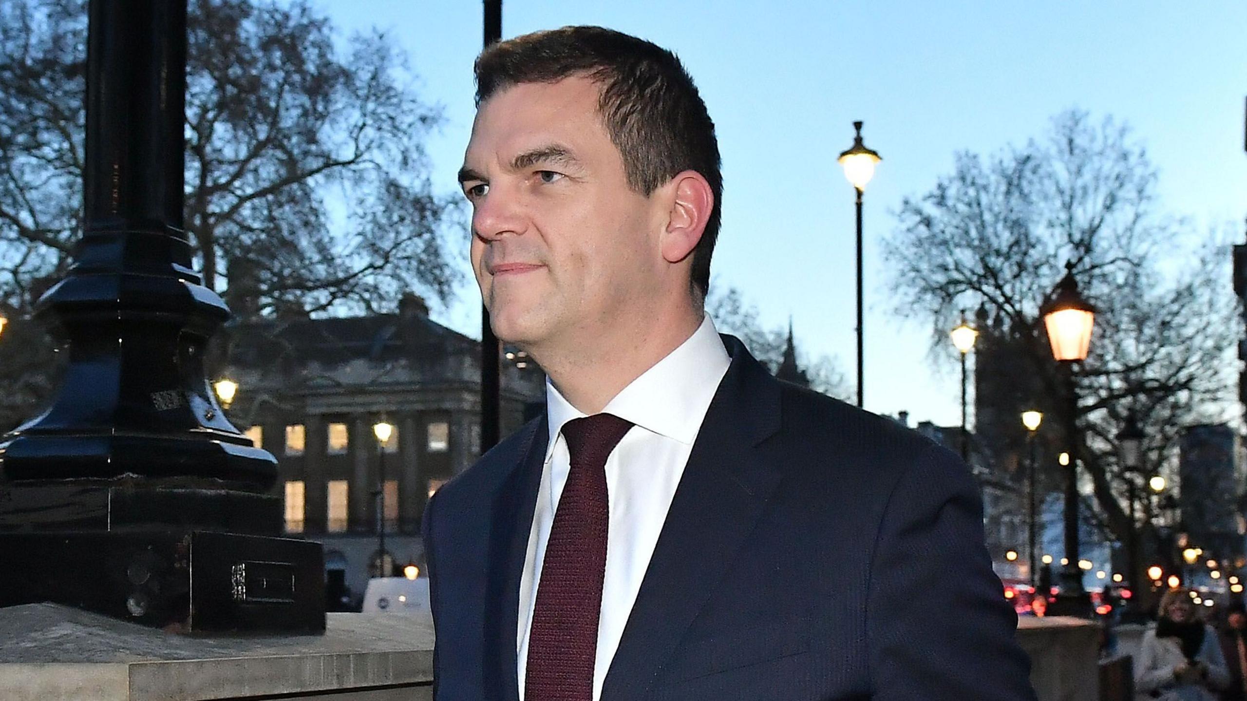 Sir Olly Robbins walking down Whitehall wearing a suit and tie.